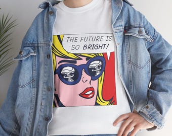 May include: White t-shirt featuring a pop art style image of a woman wearing blue sunglasses with a mushroom cloud reflection. The text "THE FUTURE IS SO BRIGHT!" is in a speech bubble. The woman has yellow hair and red lips.