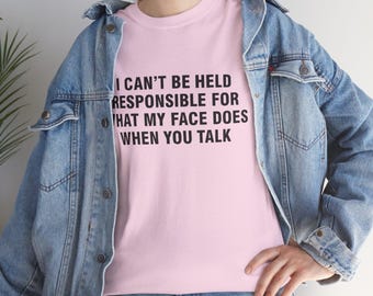 Op de afbeelding: Een lichtroze t-shirt met de zwarte tekst: "I CAN'T BE HELD RESPONSIBLE FOR WHAT MY FACE DOES WHEN YOU TALK". Het wordt gedragen met een lichtblauwe spijkerjas.