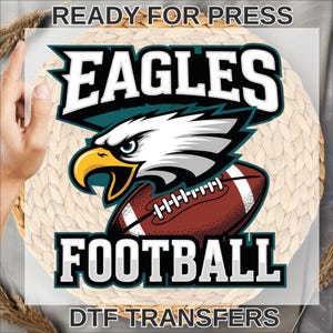 May include: A DTF transfer design featuring the word "EAGLES" in white block letters above a graphic of an eagle's head and a football. The word "FOOTBALL" is below the football. The text "READY FOR PRESS" and "DTF TRANSFERS" are also included.
