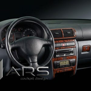 Op de afbeelding: Auto-interieur met een zwart dashboard, stuurwiel en afwerking. Het dashboard heeft houtnerfdetails rond de ventilatieopeningen, radio en console. Het logo "MARS cockpit design" is zichtbaar.