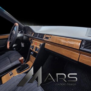 Peut inclure: Un intérieur de voiture avec un tableau de bord et une console centrale dotés d'une finition en bois brillant. L'habitacle comprend un volant avec une poignée beige, des sièges en tissu sombre et un pommeau de levier de vitesse en bois.