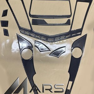May include: Carbon fiber cockpit design kit with multiple pieces. The kit includes pieces for the dashboard, center console, and door panels. The pieces are black with a carbon fiber weave pattern. The logo "MARS cockpit design" is visible.