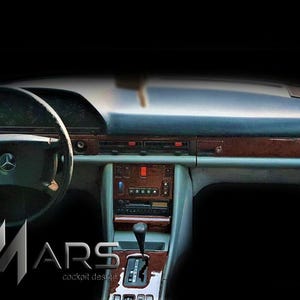 Può includere: Un interno di veicolo caratterizzato da un cruscotto scuro con finiture in legno, un volante con stemma centrale Mercedes-Benz, una console centrale con leva del cambio automatico e pulsanti per il climatizzatore. Il testo MARS cockpit design è visibile.