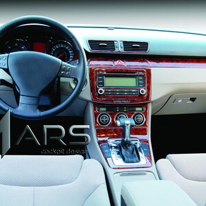 Peut inclure: Intérieur de voiture avec un volant noir, des garnitures en bois et une console centrale avec une radio et un levier de vitesses. Les sièges sont beige clair. Le logo "ARS cockpit design" est visible.