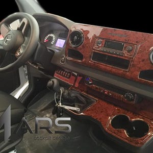May include: Vehicle dashboard with wood effect trim. The interior includes a steering wheel, gauges, radio, and air vents. The seats are black, and the design is modern. The logo "MARS cockpit design" is visible on the lower left.