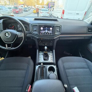 Op de afbeelding: Interieur van een Volkswagen-voertuig. Het zwarte dashboard heeft een centraal infotainmentscherm en rode sfeerverlichting. Het stuurwiel heeft een zilveren Volkswagen-logo. De stoelen zijn zwart met een textuur.