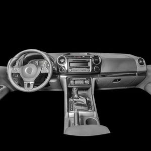 Op de afbeelding: Zwart-wit afbeelding van het interieur van een auto, met het dashboard, stuurwiel en deurpanelen. Het dashboard heeft een radio, ventilatieopeningen en diverse bedieningselementen. Het stuurwiel heeft een centraal embleem. De versnellingspook en bekerhouders zijn zichtbaar.