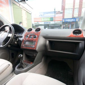 Puede incluir: Vista interior de un coche con salpicadero y asientos grises. El salpicadero presenta detalles de veta de madera alrededor de la radio y las rejillas de ventilación. El volante es negro y los asientos son de color claro.