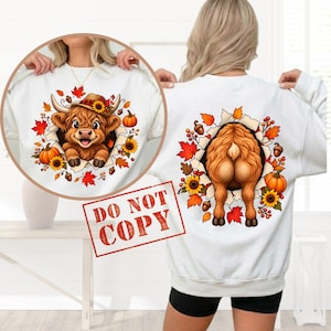 Puede incluir: Una sudadera blanca de manga larga con un gráfico de una vaca Highland. La vista frontal muestra la cara de la vaca con un sombrero, mientras que la vista trasera muestra la parte posterior, rodeadas de hojas de otoño, girasoles y calabazas.
