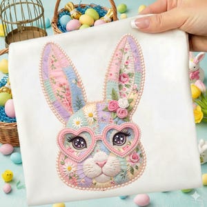 Könnte beinhalten: Ein weißer Stoff mit einem farbenfrohen Patchwork-Hasen-Design. Der Hase hat herzförmige Brille, Blumenakzente und Perlenschmuck. Das Design zeigt Pastellfarben und Blumenmuster, ideal für Ostern.