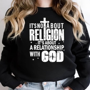 May include: Black sweatshirt with the text "IT'S NOT ABOUT RELIGION. IT'S ABOUT A RELATIONSHIP WITH GOD" in white. A white cross is above the word "RELIGION". The sweatshirt is a crew neck style.