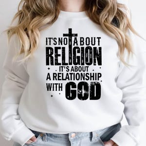 K&ouml;nnte beinhalten: Wei&szlig;es Sweatshirt mit dem schwarzen Text "IT'S NOT ABOUT RELIGION, IT'S ABOUT A RELATIONSHIP WITH GOD", mit einem Kreuz &uuml;ber dem Wort "RELIGION". Das Sweatshirt hat einen l&auml;ssigen Stil.