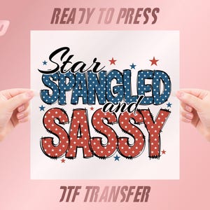 May include: A white square with the words "Star Spangled and Sassy" in red, white, and blue. The words are decorated with stars. The words "Ready to Press" and "DTF Transfer" are also visible.