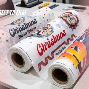May include: Three rolls of Direct to Film transfer sheets featuring various printed designs. The left roll shows Christmas patterns, the center roll displays a bulldog in a Santa hat with the text Christmas Premium Roll, and the right roll shows a large letter D.