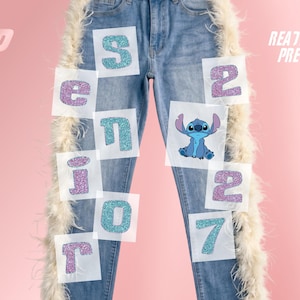 May include: Light blue denim jeans featuring white feather trim along the outer seams. The jeans display glittery iron-on transfers spelling SENIOR 2027 in alternating blue and purple letters, with a graphic of the character Stitch included.