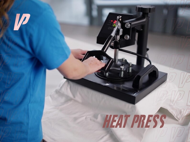 May include: A black heat press machine with a digital control panel and a sturdy metal handle, positioned over a white fabric surface. The device features a flat heating plate, vertical support column, and tension springs for even pressure application.