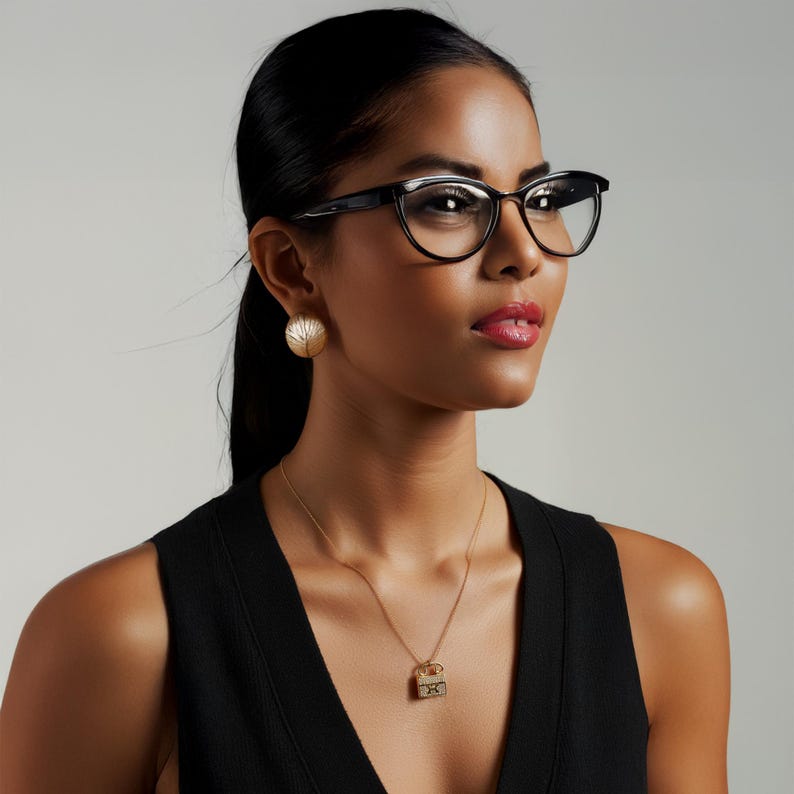 Puede incluir: Una mujer con gafas negras de ojo de gato, pendientes dorados y un collar dorado con un peque&ntilde;o colgante. La mujer lleva un top negro sin mangas. El fondo es de color gris claro liso.