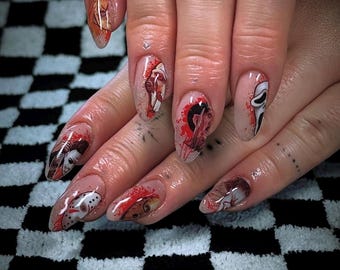 Pode incluir: Unhas acrílicas longas e ovais com desenhos de personagens de filmes de terror. A nail art apresenta imagens de Michael Myers, Jason Voorhees e a máscara de Scream, com efeitos de respingos vermelhos. As unhas são pintadas em uma mão.