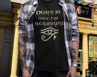 Könnte beinhalten: Ein schwarzes T-Shirt mit dem Text "DEATH IS ONLY THE BEGINNING" in einer stilisierten Schrift über einem Auge des Horus-Symbols, getragen unter einem grau-weiß karierten Hemd. Das Design ist in einer hellen, abgenutzten Farbe gedruckt.