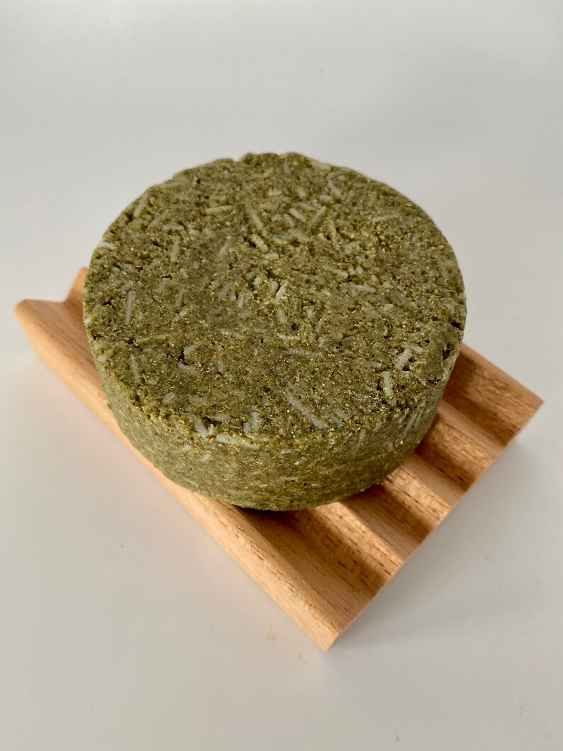 May include: A round, green and white bar of soap on a wooden soap dish. The soap is made with natural ingredients and is designed to cleanse and nourish the skin.
