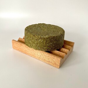 May include: A round, green bar of soap sits on a wooden soap dish. The soap dish has a wavy design.