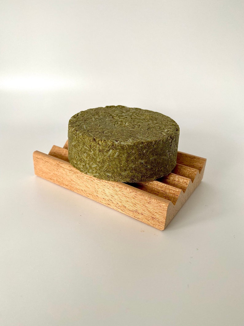 May include: A round, green bar of soap sits on a wooden soap dish. The soap dish has a wavy design.