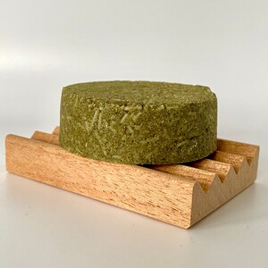 May include: A green bar of soap on a wooden soap dish. The soap is made with natural ingredients and is designed to be gentle on the skin.