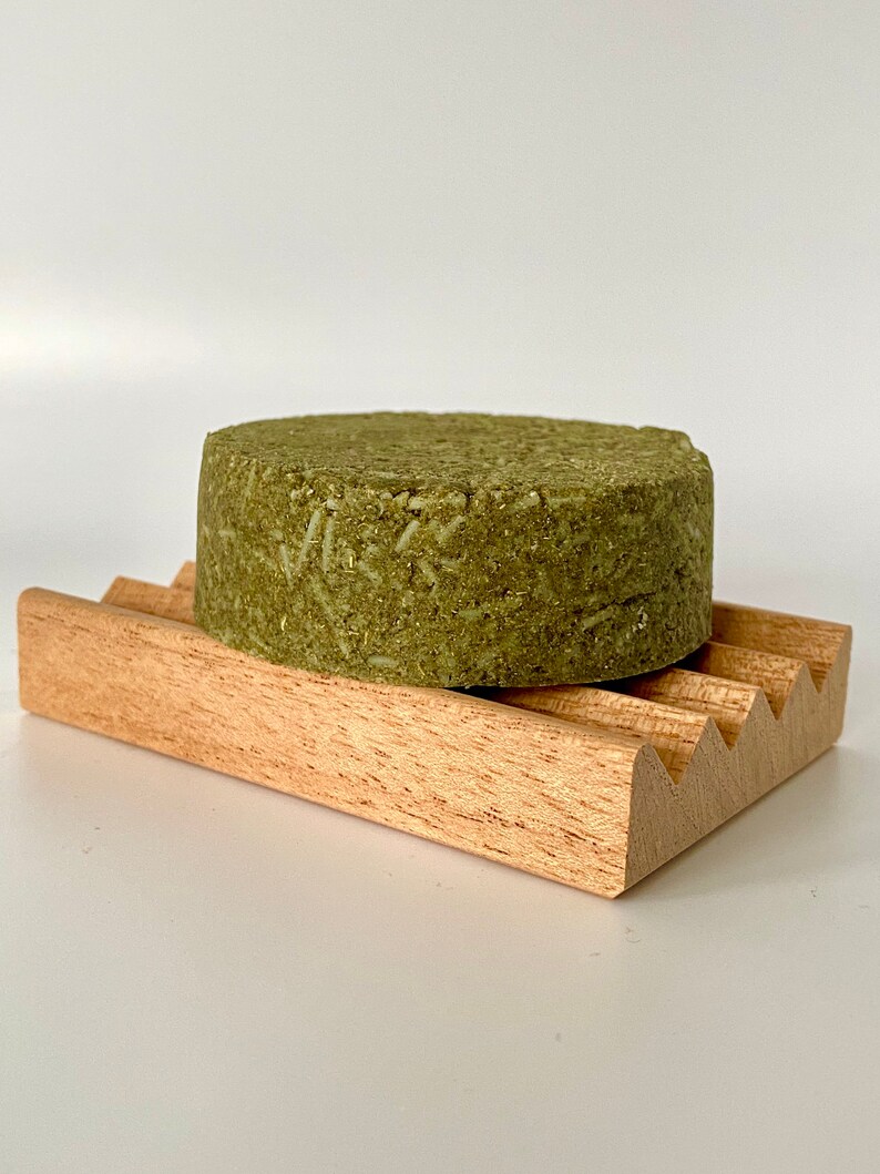 May include: A green bar of soap on a wooden soap dish. The soap is made with natural ingredients and is designed to be gentle on the skin.