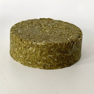 May include: A round, green, solid bar of soap. The soap has a rough, textured surface.