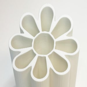 May include: A white, flower-shaped container with multiple compartments. The design features rounded petal-like sections surrounding a central circular area. The object is made of a solid, opaque material and is suitable for holding items.