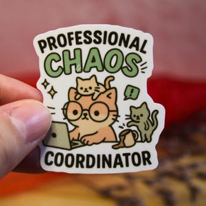 Könnte beinhalten: Ein weißer Aufkleber mit einer Cartoon-Katze, die eine Brille trägt und an einem Laptop arbeitet. Der Aufkleber trägt den Text "PROFESSIONAL CHAOS COORDINATOR" in grüner und schwarzer Schrift. Zwei weitere Katzen sind ebenfalls abgebildet.
