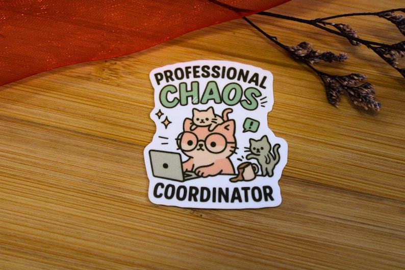 Puede incluir: Una pegatina blanca con las palabras "PROFESSIONAL CHAOS COORDINATOR". Presenta un gato de dibujos animados con gafas y un port&aacute;til, con otros dos gatos. La pegatina est&aacute; sobre una superficie de madera.