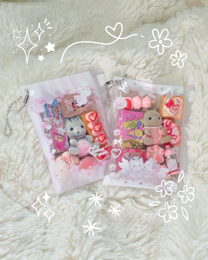 K&ouml;nnte beinhalten: Zwei transparente Beutel gef&uuml;llt mit verschiedenen rosa und wei&szlig;en S&uuml;&szlig;igkeiten, Miniatur-Pl&uuml;schtieren und Snacks. Die Beutel sind mit Blumen- und Herzmotiven verziert und liegen auf einer flauschigen wei&szlig;en Oberfl&auml;che. Ein Beutel hat eine silberne Kette.