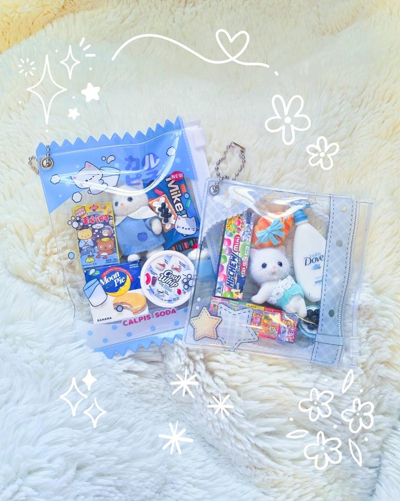 May include: Two clear, blue-trimmed pouches filled with assorted items. One contains a plush cat, snacks, and a drink. The other has a plush bear, snacks, and a drink. The pouches are on a fluffy white surface.