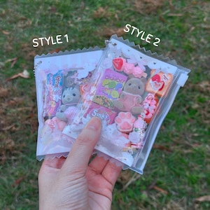 K&ouml;nnte beinhalten: Zwei transparente Plastikt&uuml;ten gef&uuml;llt mit Miniaturspielzeug und S&uuml;&szlig;igkeiten. Eine T&uuml;te ist mit "STYLE 1" und die andere mit "STYLE 2" beschriftet. Die T&uuml;ten enthalten kleine Pl&uuml;schtiere, S&uuml;&szlig;igkeiten und andere dekorative Gegenst&auml;nde. Der Hintergrund ist gr&uuml;nes Gras.