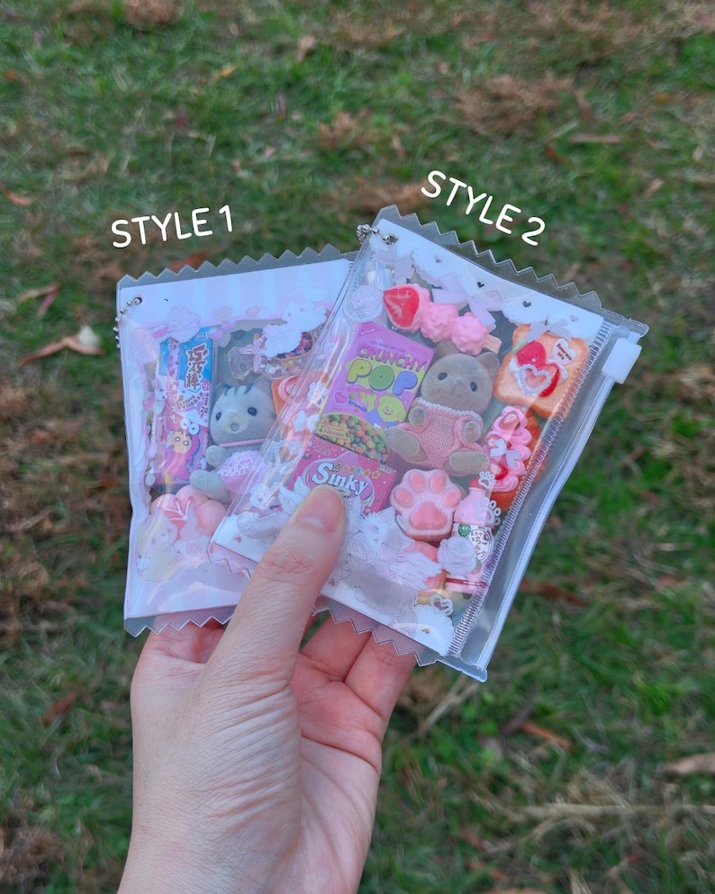 K&ouml;nnte beinhalten: Zwei transparente Plastikt&uuml;ten gef&uuml;llt mit Miniaturspielzeug und S&uuml;&szlig;igkeiten. Eine T&uuml;te ist mit "STYLE 1" und die andere mit "STYLE 2" beschriftet. Die T&uuml;ten enthalten kleine Pl&uuml;schtiere, S&uuml;&szlig;igkeiten und andere dekorative Gegenst&auml;nde. Der Hintergrund ist gr&uuml;nes Gras.