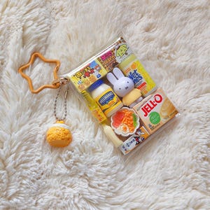 Peut inclure: Une pochette en plastique transparent remplie de miniatures alimentaires et de personnages, dont un pot de mayonnaise Hellmann's, une bo&icirc;te de Jell-O, une figurine Miffy et un petit bol de nourriture. Un porte-cl&eacute;s &eacute;toile orange est attach&eacute;.