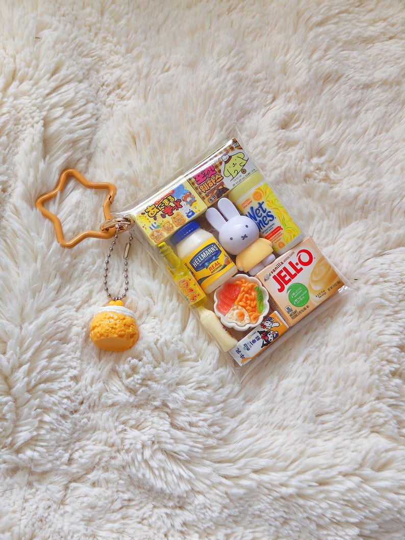 Peut inclure: Une pochette en plastique transparent remplie de miniatures alimentaires et de personnages, dont un pot de mayonnaise Hellmann's, une bo&icirc;te de Jell-O, une figurine Miffy et un petit bol de nourriture. Un porte-cl&eacute;s &eacute;toile orange est attach&eacute;.