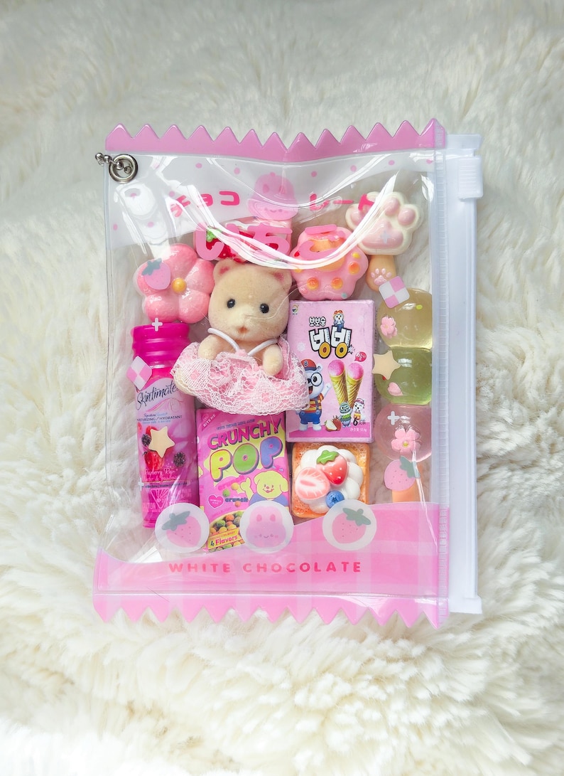 May include: A clear plastic bag filled with pink and white candies, a small bear figurine, and various miniature food items. The bag has a pink zipper and the words "WHITE CHOCOLATE" printed on it.