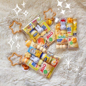 Peut inclure: Trois pochettes rectangulaires transparentes remplies de miniatures de produits alimentaires et m&eacute;nagers, incluant des bo&icirc;tes de Jell-O, de la mayonnaise Hellmann's, des lingettes Wet Ones et des figurines Miffy. Chaque pochette a un mousqueton en &eacute;toile jaune.