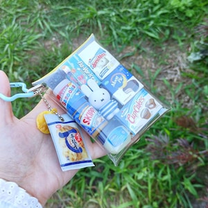 Pu&ograve; includere: Una bustina in plastica trasparente riempita con repliche in miniatura di cibo e snack, tra cui gomma Bazooka, burro di arachidi Skippy, Moon Pie, Hostess Donettes, CupCakes e una figura di Miffy. Un piccolo ciondolo a forma di snack &egrave; appeso.