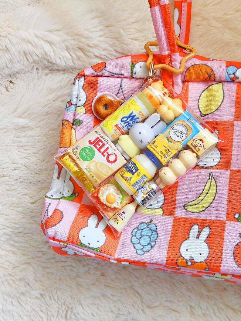 Peut inclure: Un sac fourre-tout &agrave; carreaux roses et orange avec des illustrations de lapins blancs, muni d'une pochette en plastique transparent fix&eacute;e par un clip en forme d'&eacute;toile. La pochette contient des miniatures alimentaires, dont Jell-O et Crystal Light.
