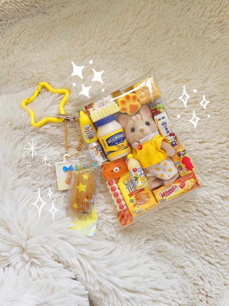 May include: A clear plastic bag filled with miniature food items, a doll, and a yellow star-shaped keychain. The food items include a bottle of Hellmann's Real mayonnaise, a bottle of yellow mustard, and a box of Velveeta cheese.
