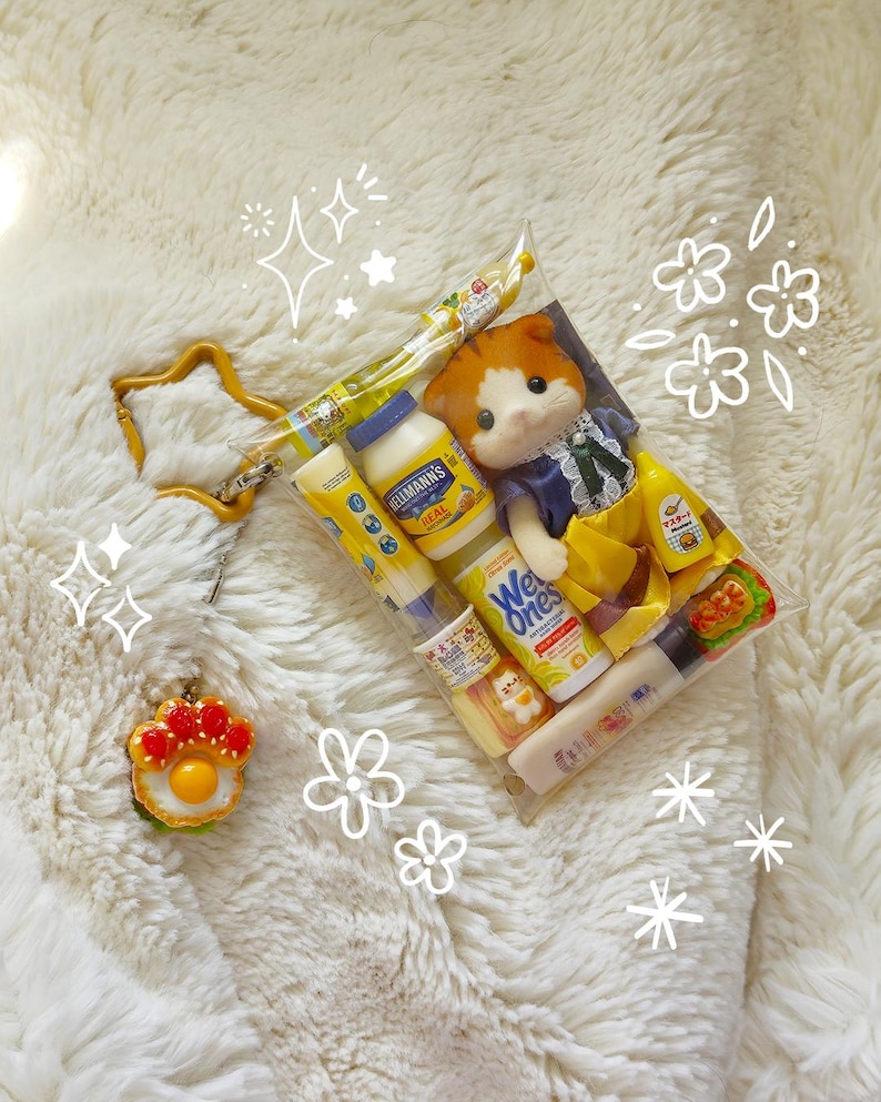 Op de afbeelding: Een doorzichtige plastic zak gevuld met miniatuurvoedsel, een kleine pop en een stervormige sleutelhanger. De zak bevat een fles Hellmann's mayonaise, mosterd en andere voedingsmiddelen. De pop is een kat met oranje en witte vacht, gekleed in een blauwe jurk.