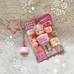 May include: A clear plastic case filled with miniature food items and a doll holding a cake that says "Happy Birthday." A pink star-shaped keychain and a small pink cake charm are attached. The case contains Pocky sticks and other treats.