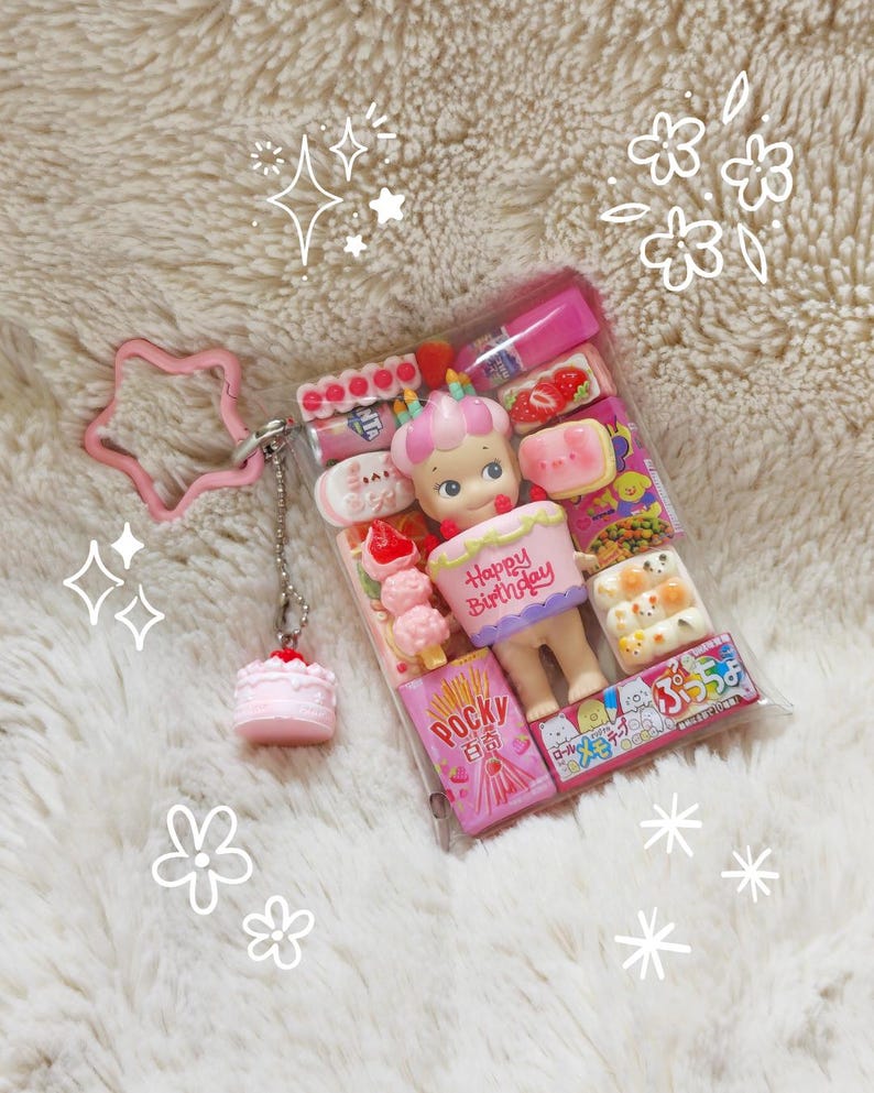 May include: A clear plastic case filled with miniature food items and a doll holding a cake that says "Happy Birthday." A pink star-shaped keychain and a small pink cake charm are attached. The case contains Pocky sticks and other treats.