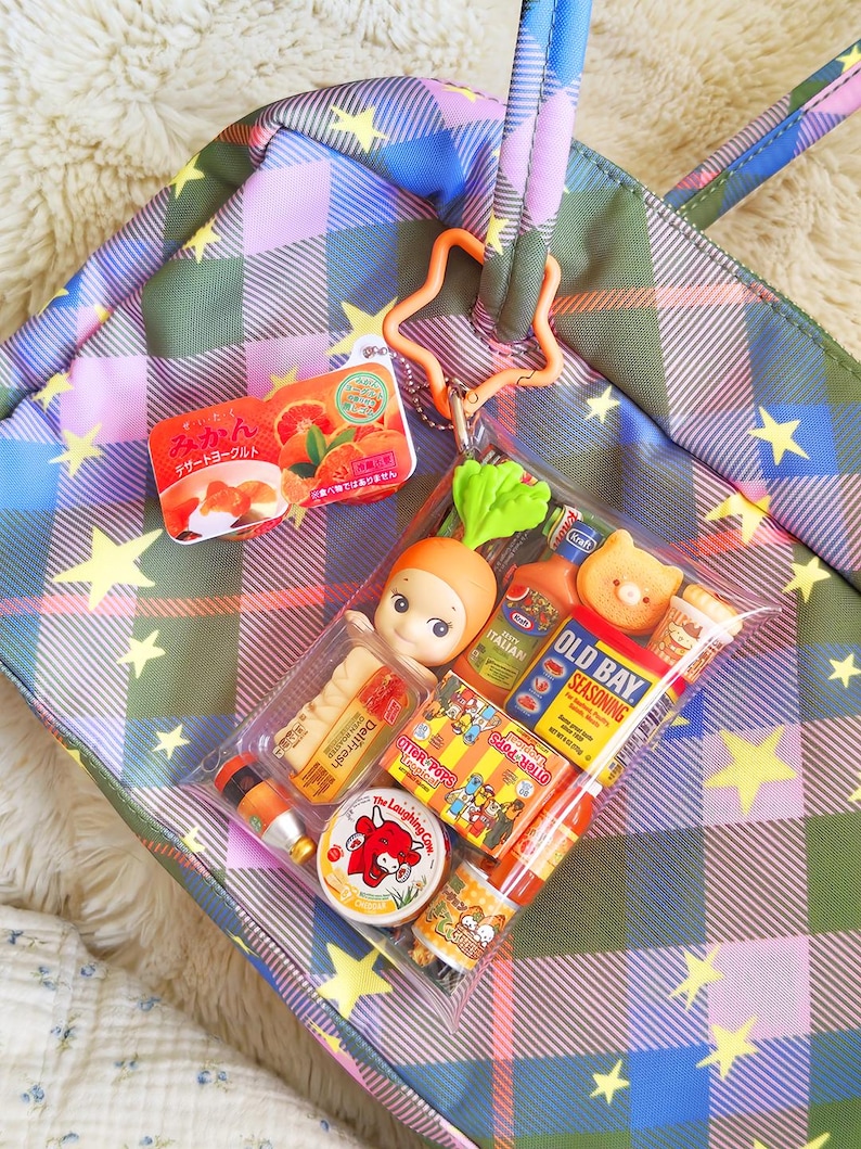 K&ouml;nnte beinhalten: Eine bunte karierte Tragetasche mit Sternmuster, die eine transparente Tasche mit Miniatur-Lebensmitteln enth&auml;lt. Enth&auml;lt eine japanische Joghurtverpackung, einen karottenf&ouml;rmigen Anh&auml;nger und verschiedene Lebensmittelminiaturen.