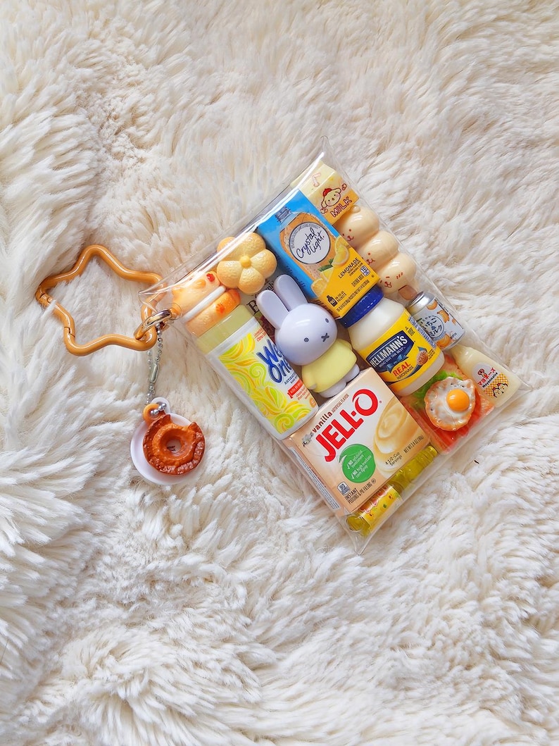Peut inclure: Une pochette en plastique transparent remplie de miniatures alimentaires et de personnages, dont une bo&icirc;te de Jell-O, de la mayonnaise Hellmann's, du Crystal Light et une figurine Miffy. Un porte-cl&eacute;s orange en forme d'&eacute;toile avec un beignet est attach&eacute;.