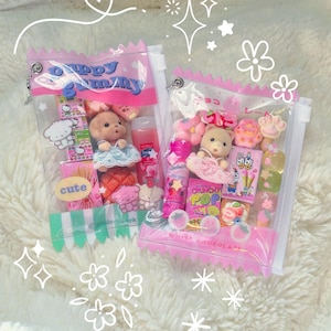 May include: Two clear, pink-trimmed pouches filled with assorted miniature toys and candies. One pouch features a teddy bear, the text "Puppy Gummy", and the word "cute". The other pouch contains a teddy bear, candies, and the text "Crunchy Pop".