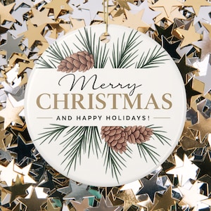 Puede incluir: Adorno navideño redondo blanco con las palabras "Merry Christmas" y "And Happy Holidays!" en oro y negro. El adorno presenta agujas de pino y piñas. Se adjunta una cuerda dorada para colgarlo.